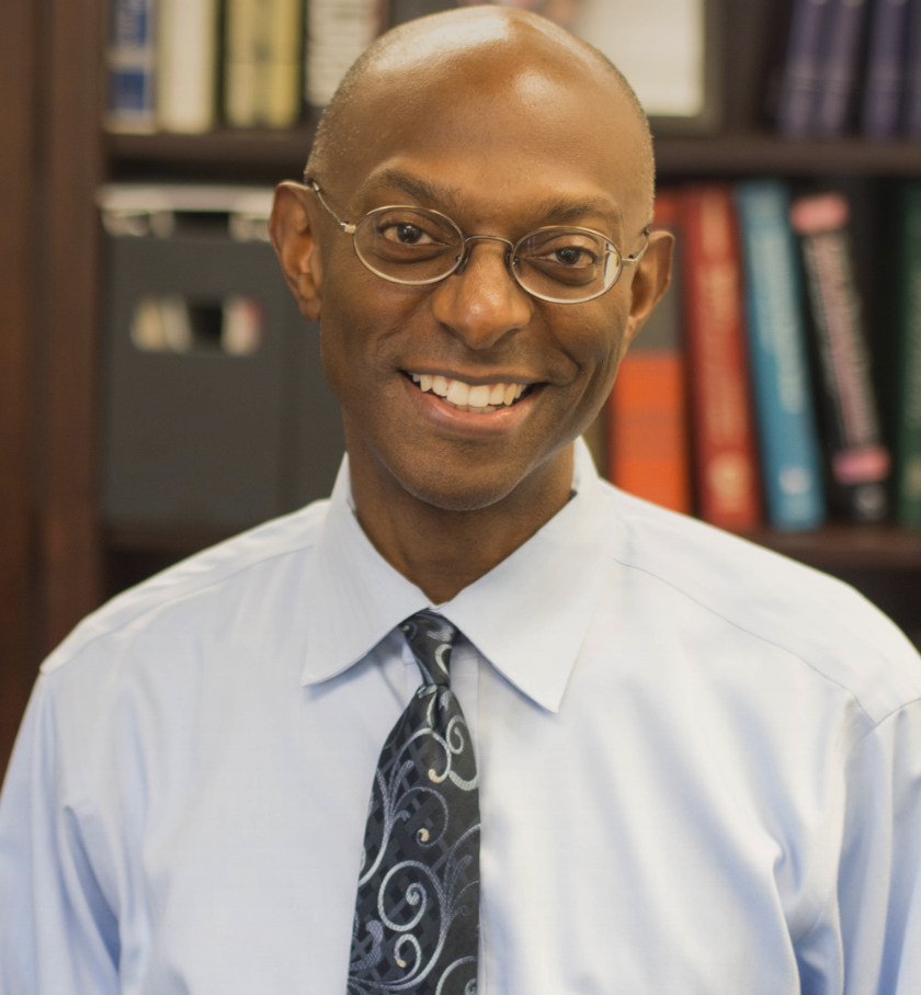 Anthony S. Welch — author, executive consultant, and speaker — smiling in a light blue shirt and tie before a wall of books